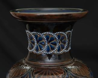 Closeup of the massive antique Royal Doulton Lambeth stoneware baluster vase, 18-1/2 inches tall. Decorated with a graceful spray of flowers over a textured pale amber ground between a band of deep blue and brown lappets and roundels at the shoulder and points with roundels at the foot, a collar of white beaded overlapping blue roundels on the neck, two bands of white beading above the foot. Base with impressed Doulton Lambeth mark, artist's marks, and model numbers. Late 19th century.