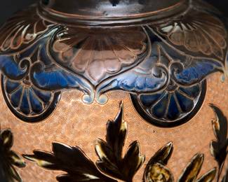 Closeup of the massive antique Royal Doulton Lambeth stoneware baluster vase, 18-1/2 inches tall. Decorated with a graceful spray of flowers over a textured pale amber ground between a band of deep blue and brown lappets and roundels at the shoulder and points with roundels at the foot, a collar of white beaded overlapping blue roundels on the neck, two bands of white beading above the foot. Base with impressed Doulton Lambeth mark, artist's marks, and model numbers. Late 19th century.