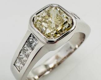 Closeup of the substantial 18k white gold ring with bezel set princess cut yellow diamond flanked with white diamonds