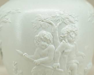 Closeup of the antique Wedgwood "Bacchanalian Boys" pitcher, white jasper, decorated with Classical imagery of young boys and satyrs in Bacchic revelry (with grapes and grape leaves in their hair.) On one side, a young Bacchus holding his thyrsus (fennel staff) is being held aloft by two other boys, a vessel of wine beside them; the other scene has a satyr and a boy sitting beneath a tree. The neck of the pitcher has applied blue sprig band of fruiting grape vines. Marked with "WEDGWOOD" to the base, dating 1790 to 1820. The design is based on drawings sent to Josiah Wedgwood by artist Lady Diana Beauclerk, née Spencer (1734-1808), daughter of the 3rd Duke of Marlborough.