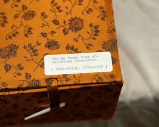 Padded fabric covered box containing a Chinese rectangular vase dating from the 1950s with wooden stand. Vase features a coral red lotus and flower tracery ground and 2 famille rose landscape scenes on the front and back. The bottom of the vase has a 4-character mark. 