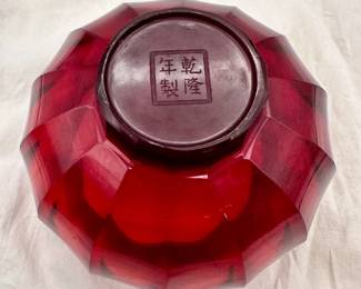Another view of the Chinese Peking Glass ruby red bowl, compressed globe form with curved, faceted sides. The base is engraved with a four-character Qianlong mark within a square.