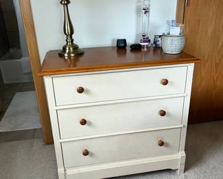 Three drawer dresser with a lamp and a few other miscellaneous items.