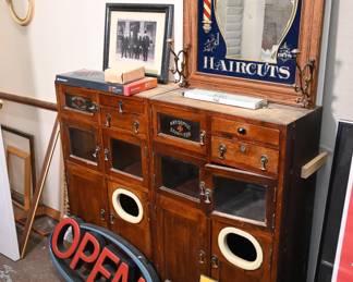 Rich oak barbershop station featuring multiple storage compartments with glass-panel doors, “ANTISEPTIC STERILIZER” enamel labels, and a striking reverse-painted advertising mirror for "Shaves and Haircuts." Authentic government-issued civil defense “Fallout Shelter” signs, dating to the 1950s–60s. These are Cold War relics with strong cultural and historical appeal.