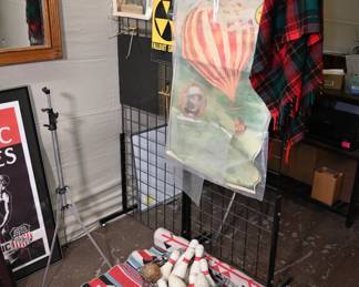 Metal wire bin filled with well-worn wooden bowling pins and two wooden balls. Poster advertising a hot air balloon event—"Astounding Extraordinary Attraction."