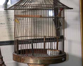 This early 20th-century hanging birdcage features a finely tapered wire dome with a heavily patinated brass base and integrated stand. The cage hangs suspended within a circular iron armature that recalls both Art Nouveau forms and early scientific apparatus. Its sculptural silhouette and original wear give it a romantic, ghostly air—equal parts aviary and relic.