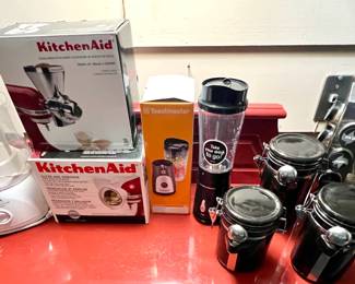 Various packaged Kitchen Aid tools and a set of 3 ceramic black canisters and a silver revolving spice rack 