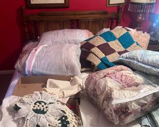 Queen size bed, quilts, pillows, and hand crafted doilies, and wall pictures.