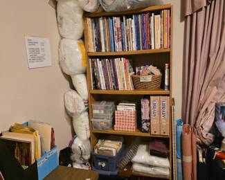 Bedroom with lots of sewing items, stuffing for pillows, pillows, non-matching set of king mattress & box springs, blankets oks & pamphlets for different kinds of sewing, cross stitch, etc.