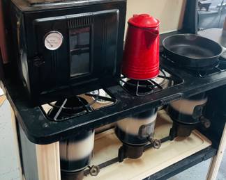 Vintage Perfection Kerosene Cookstove with Oven and Red Coffee Pot
Step into a bygone era with this vintage Perfection kerosene cookstove, complete with an oven attachment and a vibrant red metal coffee pot. This early-to-mid 20th century piece features three burners powered by cylindrical kerosene tanks below, offering reliable off-grid cooking through a classic wick system. A cast iron skillet rests ready for use, while the oven unit—topped with a heat gauge—adds to the stove’s functionality. Perfect for collectors or farmhouse-style decor, this setup brings rustic charm and practical history into any space.