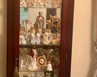 Wood and glass lighted curio cabinet filled with angels, holiday, tea cup and saucer sets.