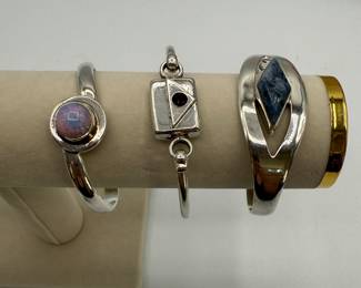 Three unique silver cuff bracelets, featuring various designs. Includes a stunning opal-set cuff, a geometric design with a denim lapis stone, and a clasped bracelet with a purple crystal. 2.20 ozt