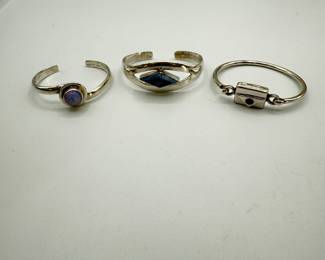 Three unique silver cuff bracelets, featuring various designs. Includes a stunning opal-set cuff, a geometric design with a denim lapis stone, and a clasped bracelet with a purple crystal. 2.20 ozt