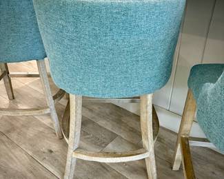Five turquoise upholstered barstools. Seat height is 24 inches. Wood leg legs with metal kick bar.
