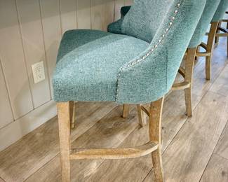Five turquoise upholstered barstools. Seat height is 24 inches. Wood leg legs with metal kick bar.