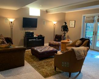 All of this lower level living room furniture is for sale(except for rug). A dark leather square ottoman, two matching upholstered chairs, an armless chair, dark brown sofa with decorative pillows, matching floor lamps,