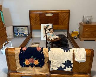 Art deco bed, antique doll in antique chair, various linens, bedside table, chest of drawers