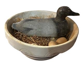 Canvasback duck decoy in a bowl with straw and eggs.