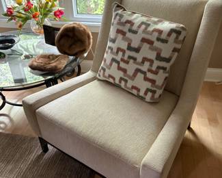 Oversized occasional chair (two available) and view of a glass round low-profile metal base cocktail/coffee table, and mink hat and purse.