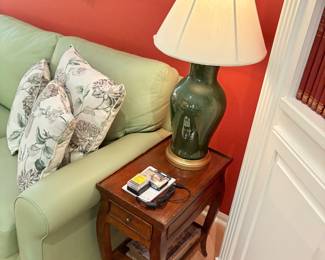 Wood side table with drawer, green lamp with red finial, and view of Leather couch