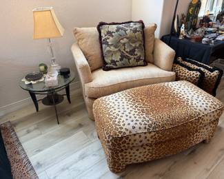 A large comfy chair and ottoman with a small glass top table and cushions