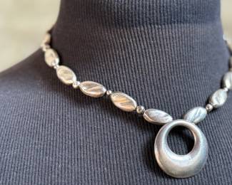 This lot features a beautiful sterling silver necklace with pendant by designer, Avi Soffer. Marked as shown in photos and measures, 18” with a total approx. weight of 48.00 grams. Avi Soffer is an Israeli jewelry designer known for his international perspective and commitment to social impact. He apprenticed with jewelry makers in Israel and Denmark, developing a unique design aesthetic. Soffer is actively involved in supporting human rights causes, including empowerment programs for Arab women in Israel and volunteering at a refugee center. He also mentors new artisans and employs individuals with disabilities in his workshop.
