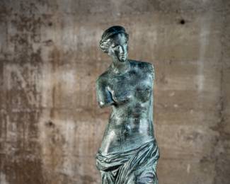 This lot features a famous replica of the Venus de Milo, one of the most famous ancient Greek sculptures. Made in Spain with maker mark near bottom as shown in photos. This sculpture is believed to be made of a hollowed bronze and measures, 24” H x 7.5” W x 7.5” D. The Venus de Milo is a masterpiece of Hellenistic sculpture and is renowned for its idealized beauty and enigmatic appeal, partly due to its missing arms.
