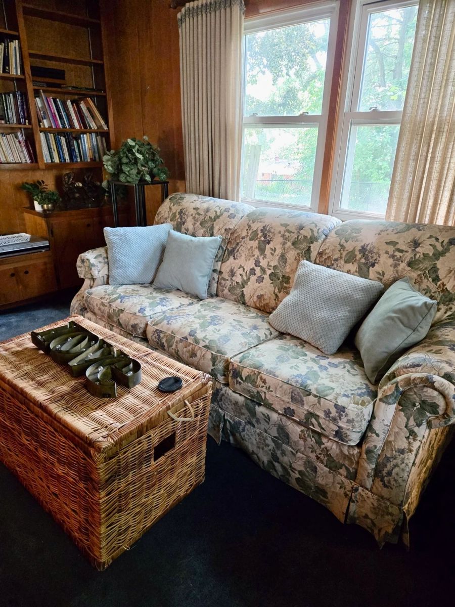 Floral Upholstered Sofa with Decorative Pillows; Wicker Trunk; LOVE Sign; Plant Stand; Silk Plants; Books