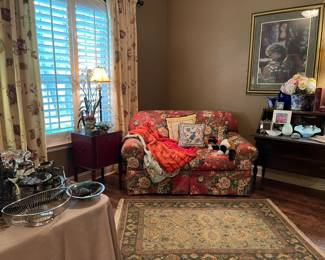 Looking into the living room, upholstered love seat with two cushions, antique writing desk, storage chest, linens and cushions