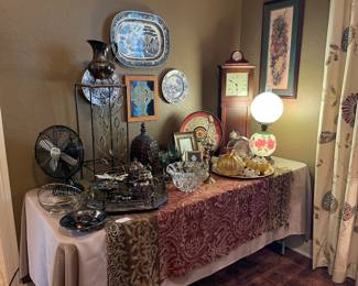 This table is in the living room and contains, vintage silver plate, cut glass, vintage Gone with the Wind lamp, clock, blue and white plates, table fan