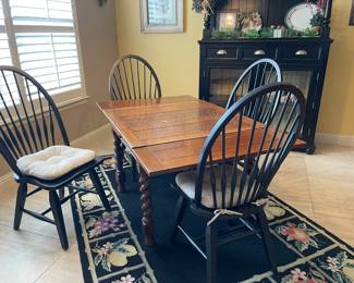 View of the oak table, four oval dining chairs, black rug with colorful fruit design
