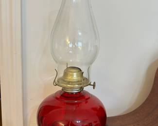 Vintage red glass oil lamp with brass burner and clear glass chimney; charming functional decor for rustic or farmhouse spaces.