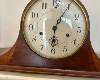 Antique wooden mantel clock with classic round face and curved base; timeless accent piece for shelf or mantle.