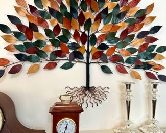 Striking mid-century metal wall sculpture depicting a tree with multicolored leaves; includes vintage shelf clock and elegant candlesticks on mantel.