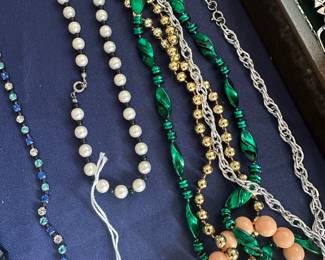 Assortment of beaded necklaces in various colors including faux pearls, green glass, blue and coral beads; vintage costume jewelry selection.