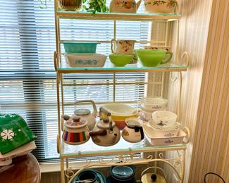 Collection of vintage Pyrex mixing bowls and kitchenware on metal shelving, featuring green, yellow and patterned nesting bowls.
