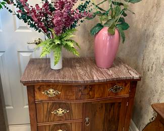 Carved wood nightstand with marble top and floral arrangement