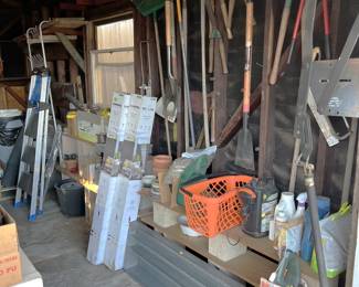 The garage has a wide selection of various stuff in it, including garden tools (hanging on the wall).