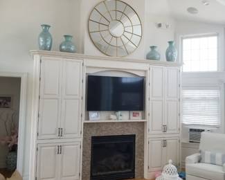 Custom cabinetry surrounds gas fireplace with remote; chic mirror and teal vases