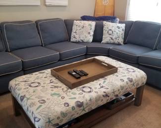 Large navy sectional sofa with white piping; ottoman/table. Note: owner keeping surfboard