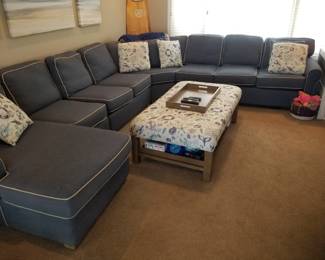 Large navy sectional sofa with white piping; ottoman/table. Note: owner keeping surfboard