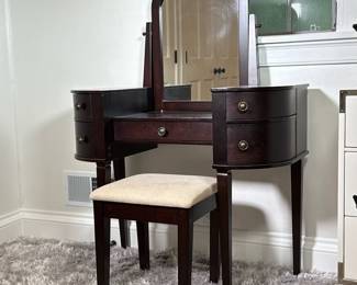 Vanity Table & Stool | Vanity mirrored makeup table in a dark wood finish with matching upholstered stool, having curved slide out compartments flanking a central drawer, with mirror - h. 33 x w. 38 x d. 18 in (table)