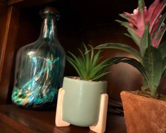 Small faux plants in ceramic pots and decorative glass bottle on wood shelf