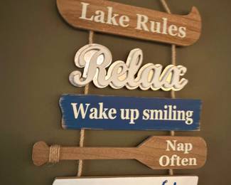 Wooden "Lake Rules" sign with hanging paddles and phrases: Relax, Wake up smiling, Nap often, Jump in the Lake