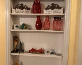 White wall shelves with assorted decor: red glass jars, figurines, signs and small collectibles