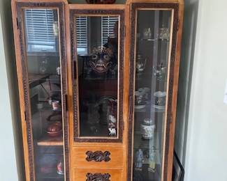 Teak display cabinet, origin Southeast Asia. Intricate hand-carved trim around 3 working doors and drawer handles. Lighting feature inside makes for a dazzling nighttime display of your treasures.