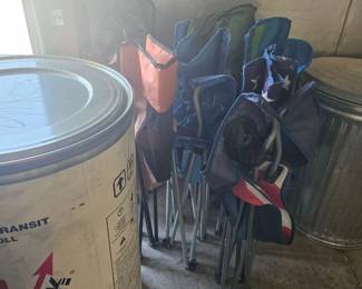 Assorted golf clubs in a stand next to a large paint bucket and metal trash can.