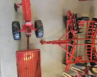 Overhead view of a red toy tractor with multiple farming implements such as cultivators and trailers lined up.