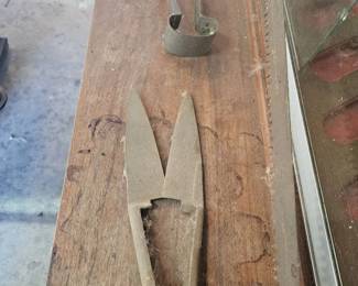 Vintage metal tools including large shears and other antique hand tools displayed on a wooden board.