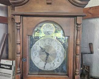 Antique wooden grandfather clock with ornate carved crown and glass front showcasing the clock face and pendulum.